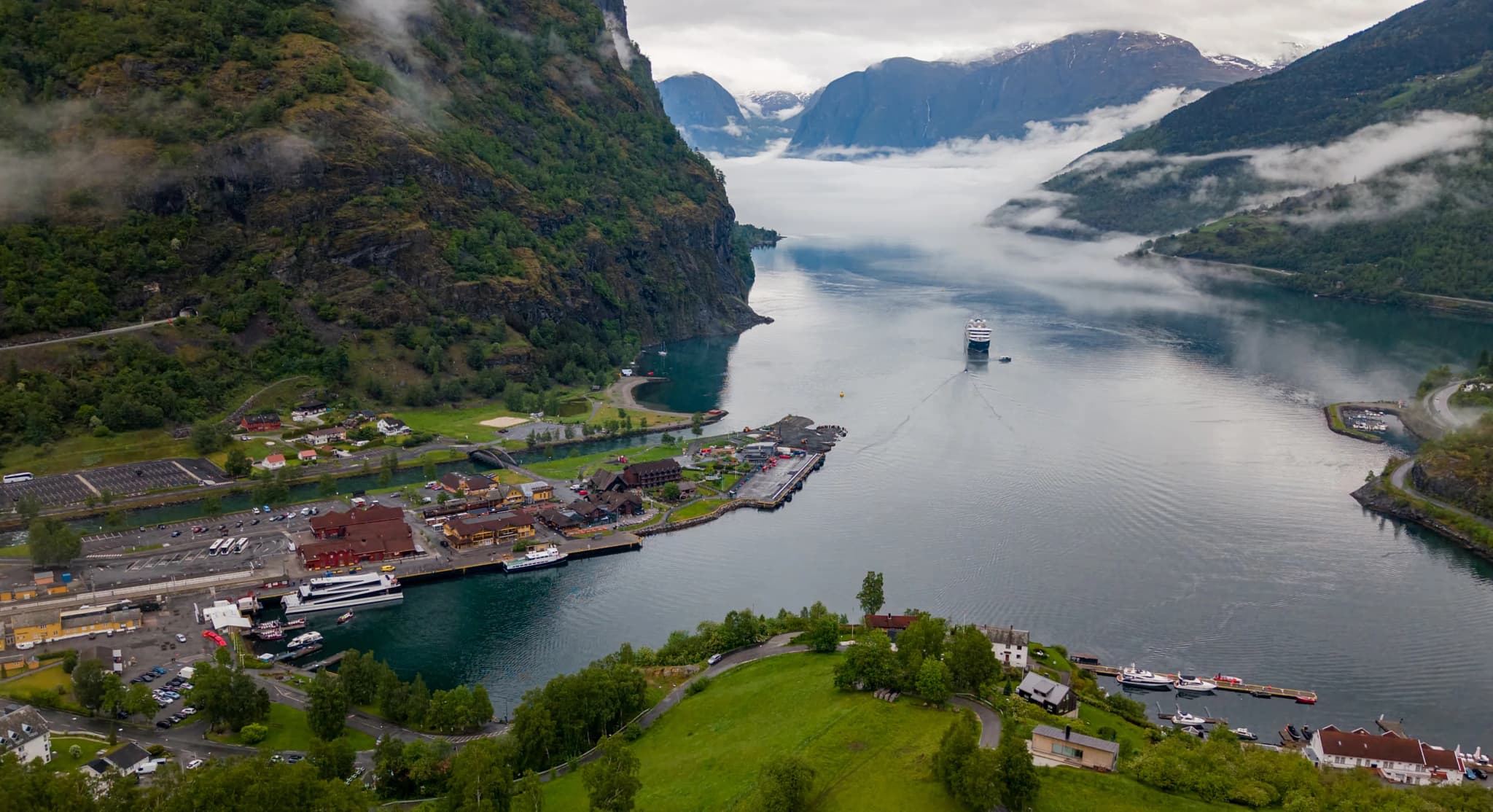 SH ship sailing into a Norwegian fjord below cloud-wrapped peaks